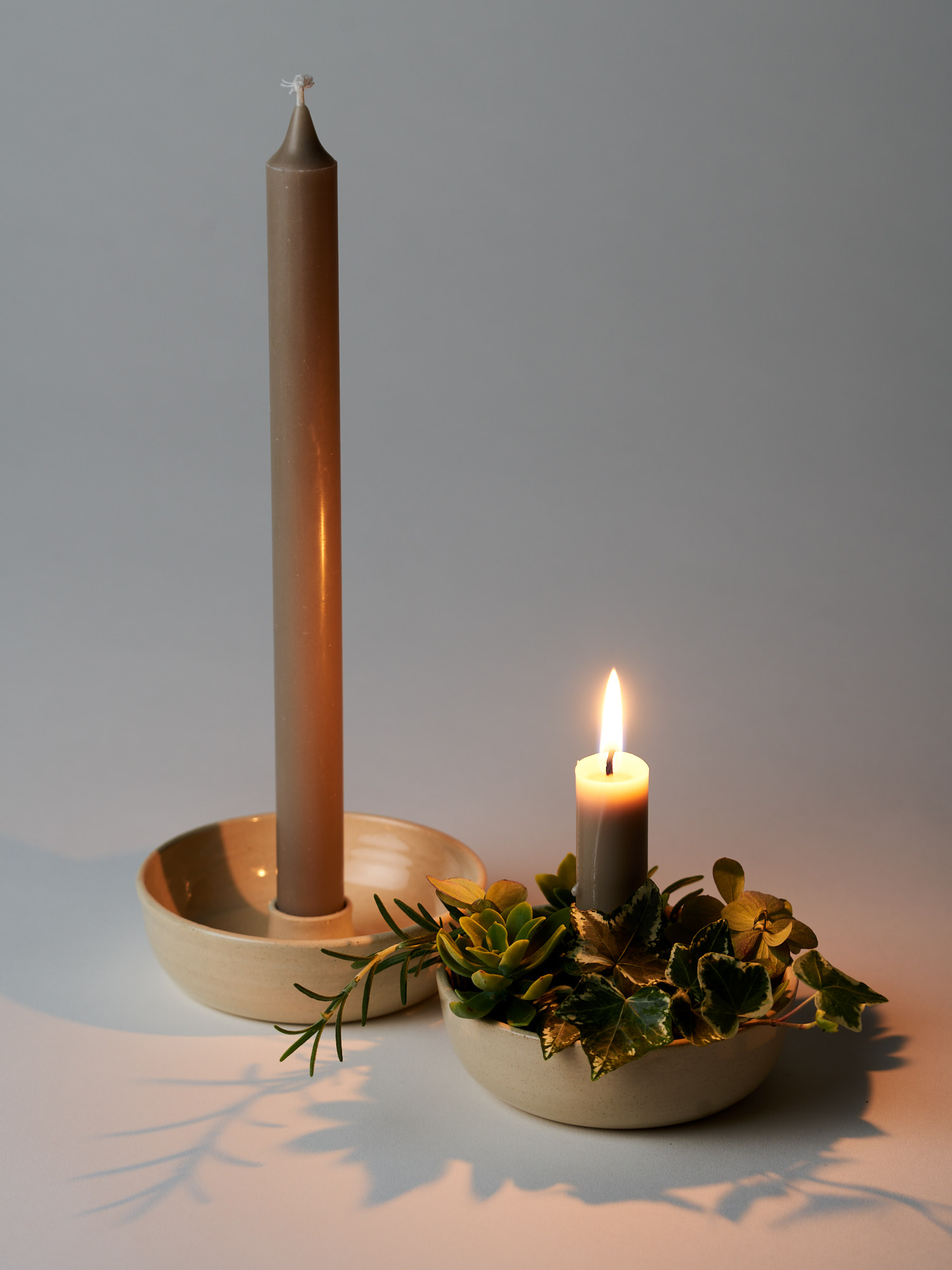 Due candelabri in gres color burro affiancati con candela accesa