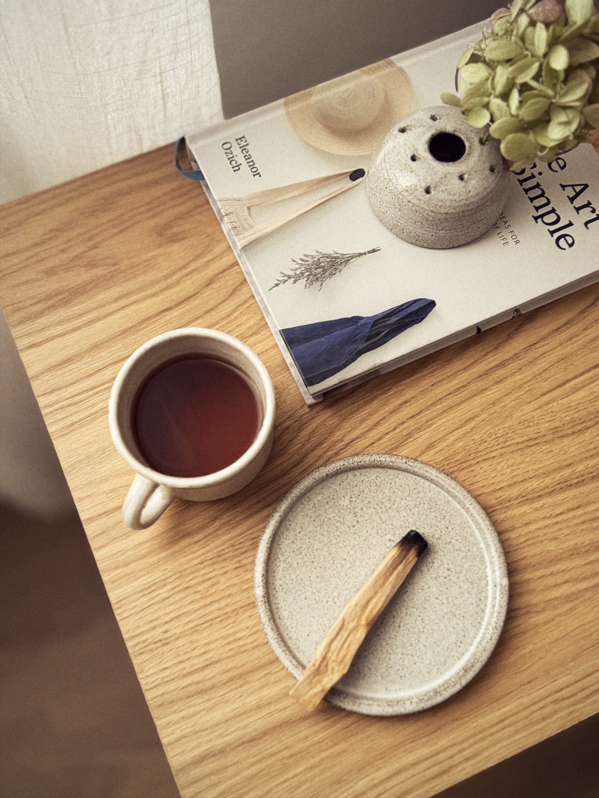 Piattino in gres con palo santo su un tavolo in legno, accanto a una tazza, un libro e un vaso con fiori.