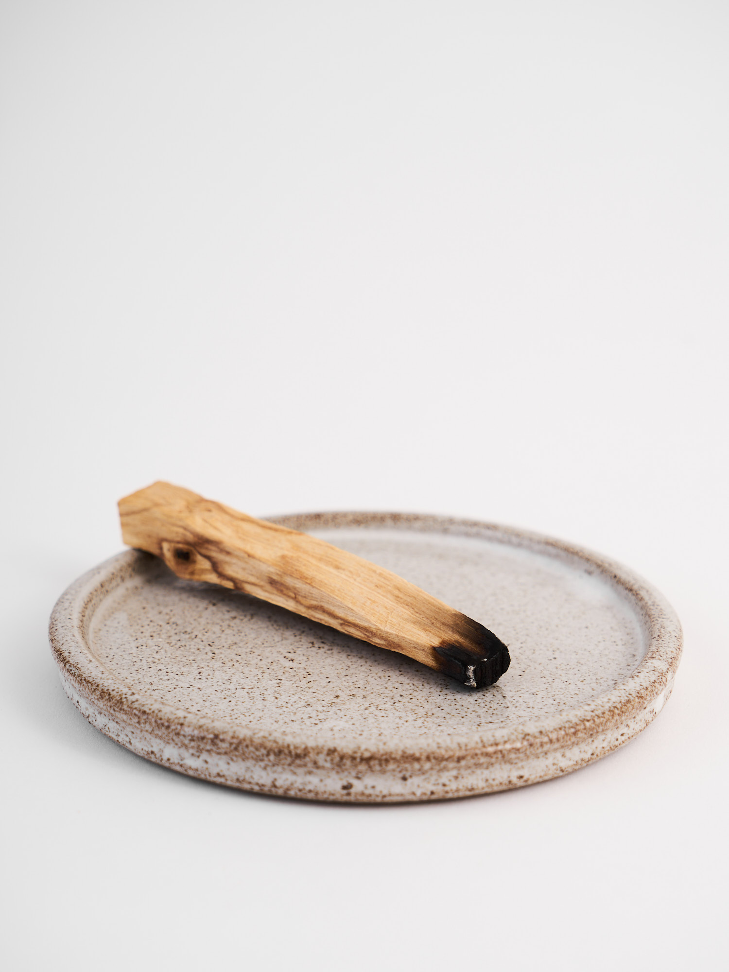 Primo piano del palo santo appoggiato sul piattino in gres smaltato puntinato.
