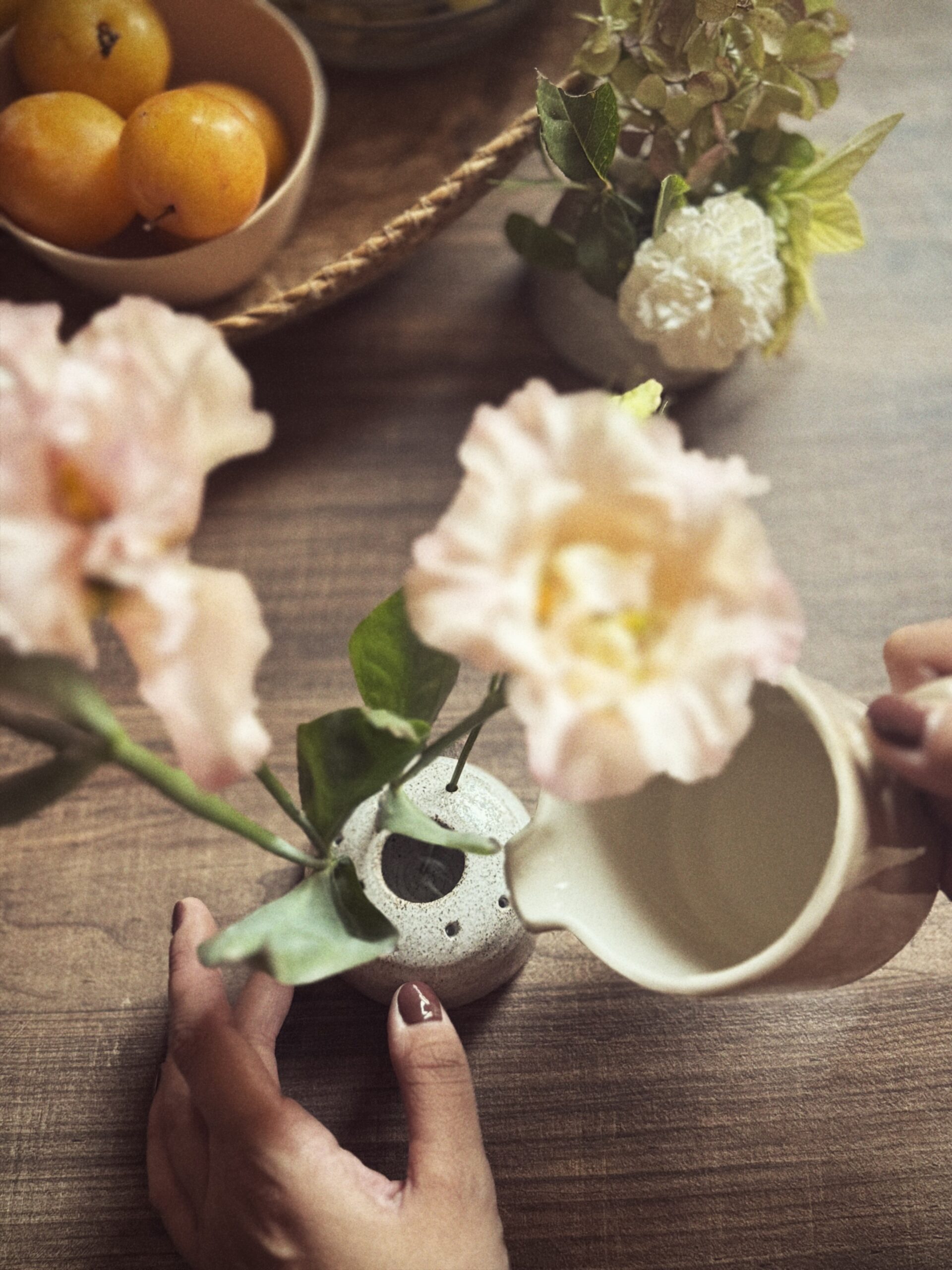 Mani che versano acqua nell’apertura centrale di un vaso portafiori in gres puntinato con fiori rosa.
