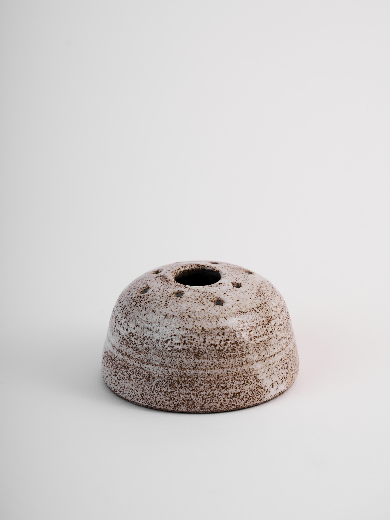Vaso portafiori basso e arrotondato in gres puntinato, senza fiori, su fondo chiaro.